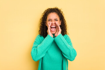 Young Brazilian curly hair cute woman isolated on yellow background shouting excited to front.