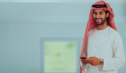 Young modern Muslim Arabian businessmen wearing traditional clothes while using smartphones at home. 