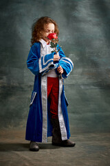 Little charming girl with curly hair in image of little prince standing with rose over on dark...