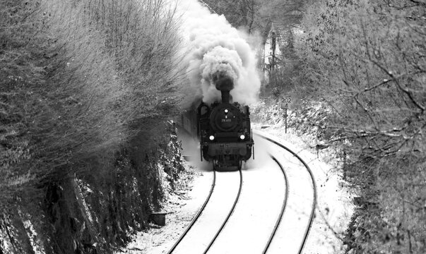 Steam train in winter season on the “Ruhrtalbahn“ (Ruhr valley line) between Arnsberg and Winterberg Sauerland Germany. Black and white vintage with white puff of smoke in picturesque rural scenery.