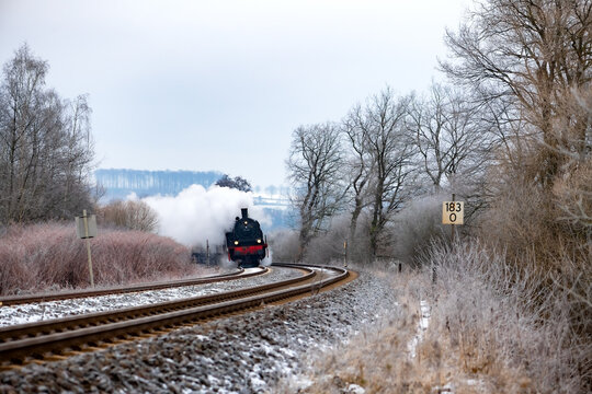Steam train winter scenery pano on the “Ruhrtalbahn“ (Ruhr valley line) in Wickede between Schwerte and Arnsberg Sauerland Germany. Vintage locomative with white puff of smoke in picturesque scenery.