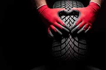 Abwaschbare Fototapete Autos Car tire service and hands of mechanic holding new tyre on black background with copy space for text