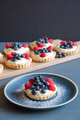 Assorted raspberry and blueberry tarts on a blue table in front of a grey background.