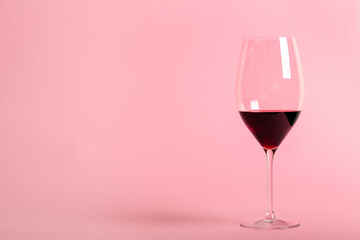 Horizontal photo of glass of red wine on light pink background