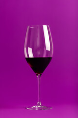 Elegant wine glass with tasty red wine on violet background
