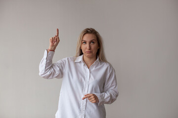 Fototapeta premium A young woman in a white shirt points up. White background.