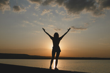 The silhouette of young sexy girl enjoying the sundown with raised up hands at the Italian lake beach 