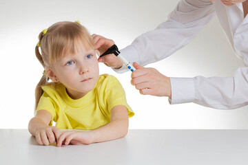 Doctor ENT doctor looks into the ear of a beautiful girl patient at the age of 5 years. Diagnosis of ear diseases in children, background, close-up - obrazy, fototapety, plakaty