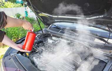 The driver of the car directs a powder fire extinguisher at the engine compartment of the car in...