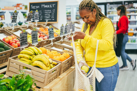 African female customer buying organic food fruits inside eco fresh market - Focus on box of oranges