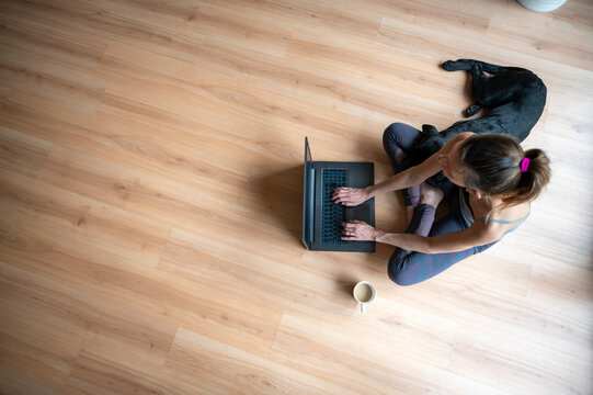 Overhead view of a young woman sitting on living room floor using laptop computer