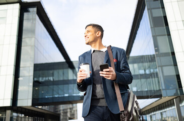 Businessman outside building with phone, coffee and bag, happy waiting for online taxi service after work. Office, business and success, man with smile holding 5g smartphone standing on city street.