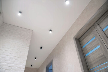 Lots of modern LED spotlights on the stretch ceiling in the hallway. Beautiful lighting, gray interior doors. Interior