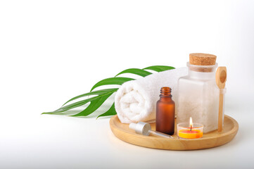 Spa treatment setting with aroma oil, spa salt bottle, rolled towel and green leaf on wooden tray