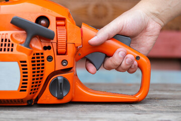 The man's hand presses the gas button in the chainsaw. The concept of adjusting the chainsaw...