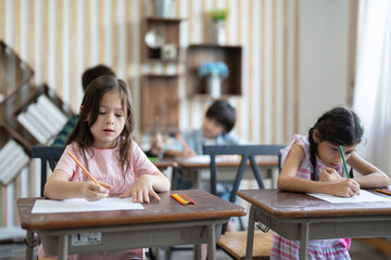 Cute little girl using color pencil drawing on paper in art study class at elementary school. Group diverse student to listen teacher in classroom . Children education and learning concept.