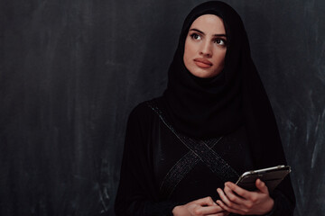 Young modern muslim business woman using tablet computer wearing glasses and hijab clothes in front of black chalkboard