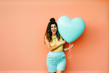 A young beautiful girl who looks like a model in the city center, in front of pastel wall background in a love costume with a huge heart shaped balloon. Illustration. Generative AI.