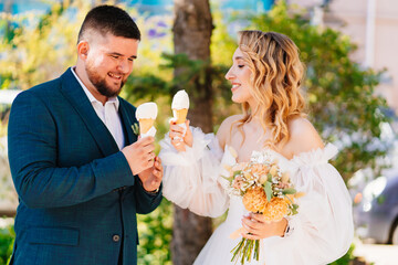 Happy and beautiful bride and groom eat ice cream outside.