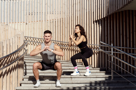 Couple doing squats on city street stairs with focused faces