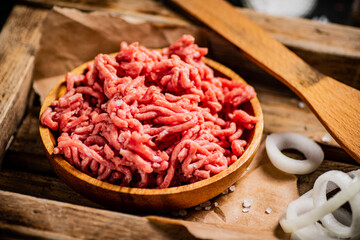 Minced meat on a wooden tray with onion rings. 