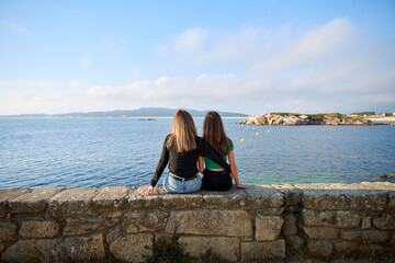 mother and daughter on their backs sitting on a stone bench looking at the sea