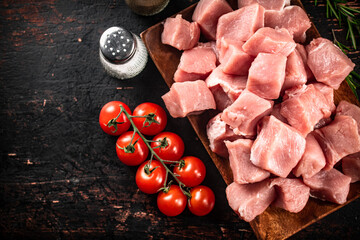 Pieces of raw pork on a wooden plate with spices and tomatoes. 