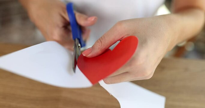 Female hands are cut out of paper red heart