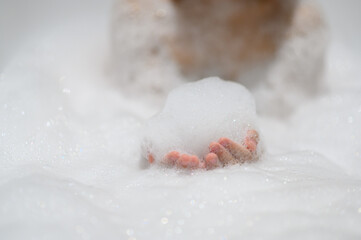 Close-up bubble foam on boy hands surrounded by soap suds when taking a bath in bathtub. Funny, healthcare lifestyle and hygiene concept.
