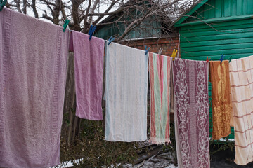 Washed towels hang and dry in the winter on a line in a village yard. Linen is fastened with plastic clothespins. A green wooden house made of boards is visible.