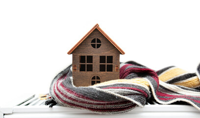 The little wooden house wrapped in the scarf lying on the radiator in the house on a transparent...
