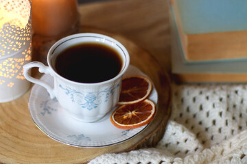 Vintage books, reading glasses, e-reader, cup of tea, bowl of biscuits and lit candle on the table. Selective focus.