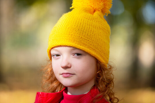 Girl in a yellow knitted hat in autumn. Portrait of a child in the autumn park.