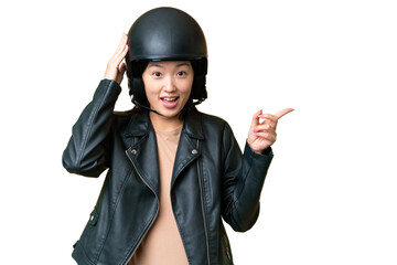 Young Asian woman with a motorcycle helmet over isolated chroma key background surprised and pointing finger to the side