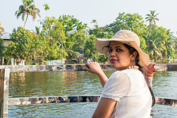 Attractive and Happy woman or lady with hat enjoys her tropical vacation on backwater of alleppey...