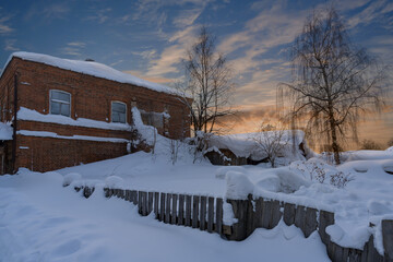 High snowdrifts wrapped a fluffy blanket around a wooden fence and an old brick house.