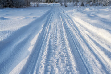 A country road running over the horizon with traces of a snow scooter. Close-up