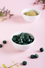 Detox products. Spirulina seaweed in pills and matcha tea powder in bowls on a pink. Vertical view