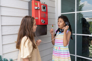 Children stand at coil red telephone box holding a telephone handset and wait for a phone call