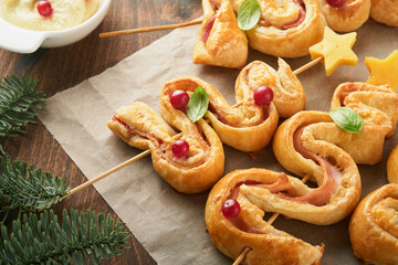 Christmas or New Year appetizer. Christmas tree shape puff pastry buns with cheese and ham. Group of Christmas tree shapes on wooden board. Festive idea for Christmas or New Year dinner. Top view.