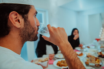 Eid Mubarak Muslim family having Iftar dinner drinking water to break feast. Eating traditional food during Ramadan feasting month at home. The Islamic Halal Eating and Drinking at modern western Isla