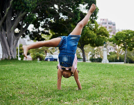 Cartwheel, child and outdoor park fun of a girl in summer with freedom and happiness. Fun, happy and holiday play of a young kid on green grass in nature on a morning with blue sky and smiling