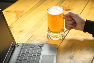 mug with beer in hand next to laptop - 563938566