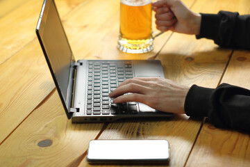 person typing on a laptop while holding a mug of beer