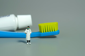 Miniature people toy figure photography. Mouth and teeth health. A female dentist doctor standing with toothpaste and toothbrush. Isolated grey background.