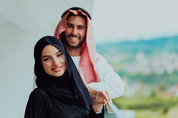 Portrait of young arabian muslim couple in traditional clothes standing on balcony representing modern islam fashion and ramadan kareem concept