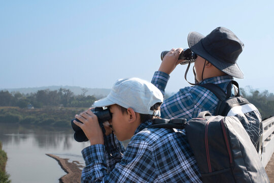 Asian boys are using binoculars to do the birds' watching in tropical forest during summer camp, idea for learning creatures and wildlife animals and insects outside the classroom.