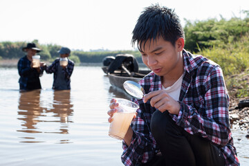 Asian boys are collecting river water samples in transparent containers to measure pH and monitor...