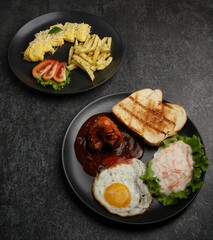 Sunny side up eggs, baked bun, vegetable salad, sausage and omelette on white plate