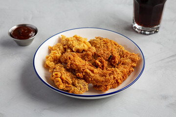 Chicken Popcorn, Wings and Tenders with BBQ Sauce on a plate on a gray background, side view.